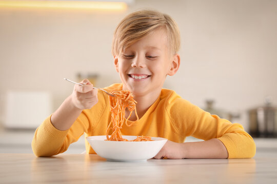 Happy boy eating tasty pasta at table in kitchen - Powered by Adobe