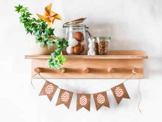 Easter kitchen interior decoration still life. Wooden shelf with a homemade flower, ceramic rabbits, eggs and homemade paper easter garland on a light background