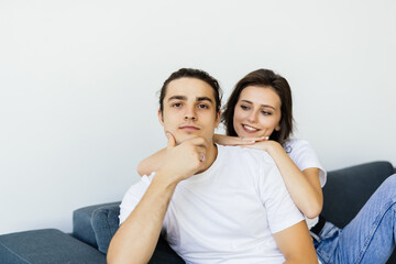 Fototapeta premium Beautiful young couple is talking and smiling while sitting on sofa at home.