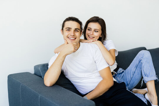 Beautiful young couple is talking and smiling while sitting on sofa at home.