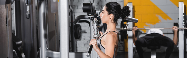Fototapeta na wymiar Young middle east woman training on lat pulldown machine in sports center, banner.