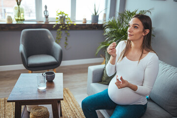 Pregnant woman sitting at a living room of a house with people, introducing a nasal swab in the...