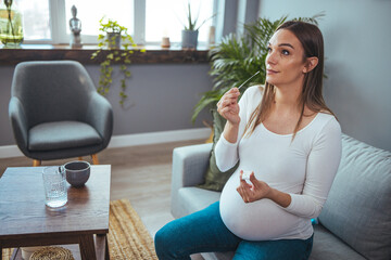 Pregnant woman sitting at a living room of a house with people, introducing a nasal swab in the...