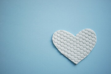 White fabric heart on pale blue table. Art card.