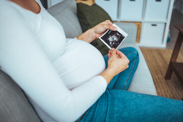 Pregnant woman looking at her baby sonography. Happy expectant lady enjoying first photo of her unborn child, anticipating her future life..