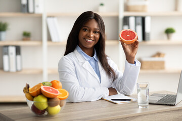Friendly black female dietitian holding grapefruit and smiling at camera, offering online weight...