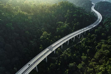 Fotobehang aerial shot of  car using elevated highway road across a green forest in the morning with mist © Kencana Studio