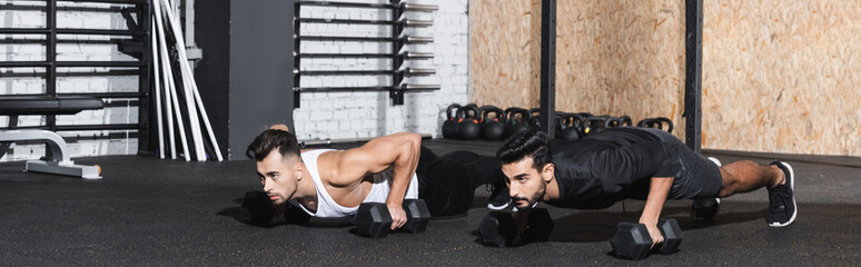 Fototapeta na wymiar Young interracial friends doing press ups with dumbbells in gym, banner.