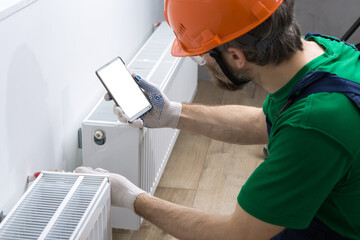 A male plumber installs a radiator in the heating system of an apartment. The guy looks at the...
