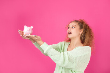A cute young girl with curly red hair holds a piggy bank, a pink piglet in her hands. The concept of wealth and safety of money.