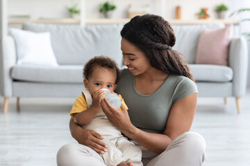 Baby Care. Loving Black Mom Giving Water Bottle To Her Toddler Son