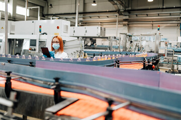 Beautiful female worker in workwear and with protective mask on her face working in bottling factory. Inspection quality control.