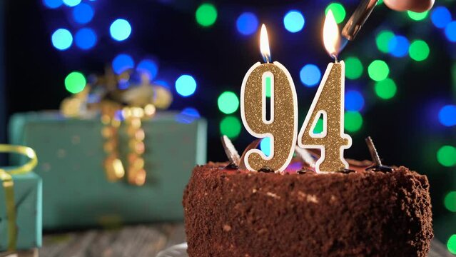 Number ninety-four birthday candle on a sweet cake on the table, 94th birthday. Fire from the lighter, blow out the holiday candle.