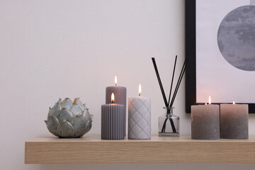Burning candles and air freshener on wooden shelf indoors
