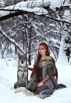 Female viking  with painted face and grey wolf in winter forest. Fantasy portrait of warrior girl