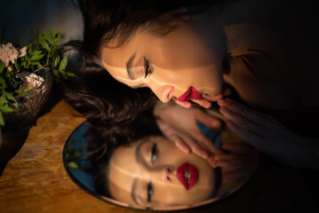 Girl fashion portrait looks in mirror. Attractive young brunette with red lips. Female self love,...