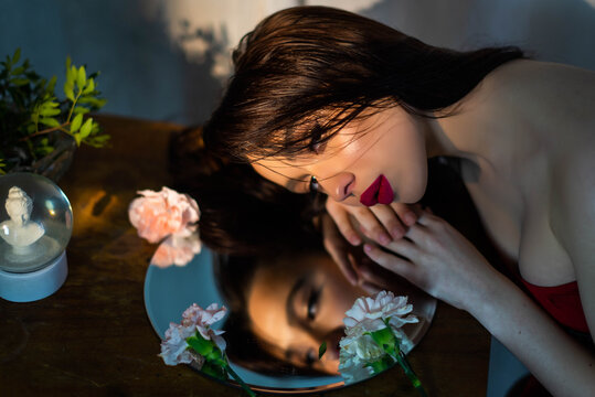 Girl fashion portrait looks in mirror. Attractive young brunette with red lips. Female self love, esteem and confidence. Believe in yourself. Plastic surgery, beauty, makeup