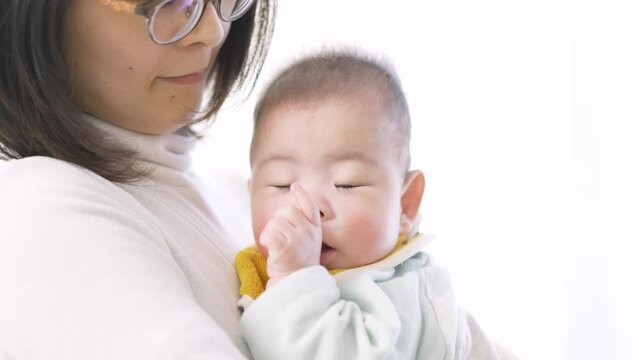 抱っこされて指をしゃぶるアジア人の赤ちゃん