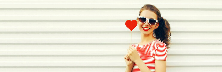 Portrait of happy smiling young woman with red sweet heart shaped lollipop on white background