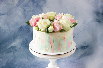 Modern wedding cake with pink and white fresh roses on cake stand. Blue background. Cake design template with space for text