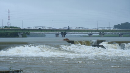 豪雨で増水した河川。橋を渡る車。