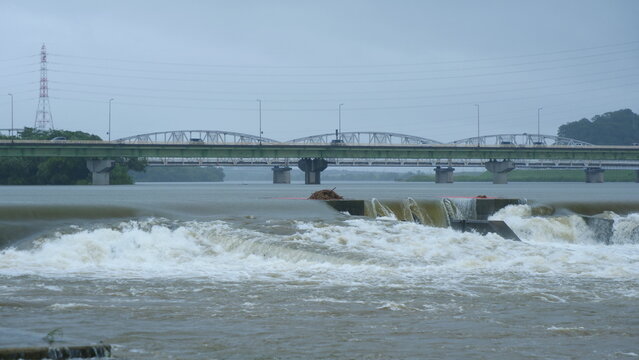 大雨の後に茶色い泥水が激しく流れる猛烈な川。豪雨で増水した河川。橋を渡る車。4K