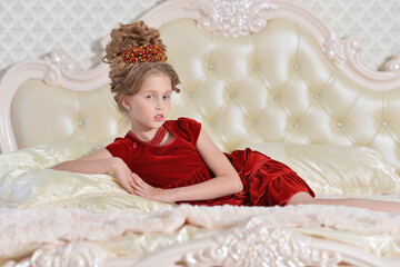 Fototapeta premium cute little girl in red dress lying on bed