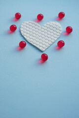 Fototapeta premium Round red vitamins around white fabric heart on blue table.