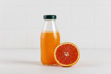 Juice of red orange in glass bottle. Freshly squeezed juice on white background. Mock up for packaging and menu