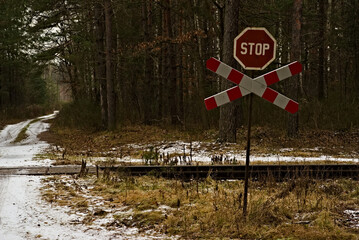 Znak stop i krzyż świętego Andrzeja przed przejazdem kolejowym w lesie zimą . Tory kolejowe , leśna droga śnieg.