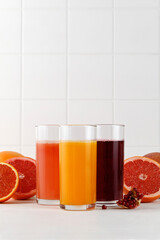 Three Freshly squeezed juices in glass on white table. Red orange, grapefruit, pomegranate juice...