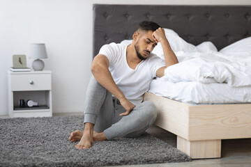 Mental Illness Concept. Depressed Young Arab Guy Sitting On Floor Near Bed