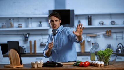 excited man singing and holding soup ladle near table with fresh ingredients.