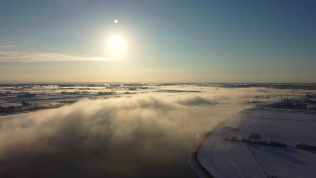 Foggy winter sunrise over the river IJssel with a high water level and ice and snow during a cold day in The Netherlands. Aerial drone point of view.