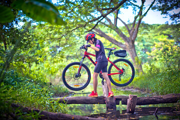 Fototapeta na wymiar woman cyclist in action of carry owns mountain bicycle crossing the small clack of ditch canal in the jungle forest, extreme riding sport trail in the route of competitive area