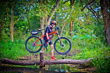 Fototapeta na wymiar woman cyclist in action of carry owns mountain bicycle crossing the small clack of ditch canal in the jungle forest, extreme riding sport trail in the route of competitive area
