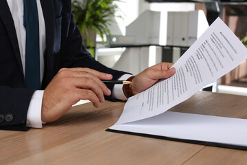 Man signing Real Estate Purchase And Sale Contract at wooden table indoors, closeup