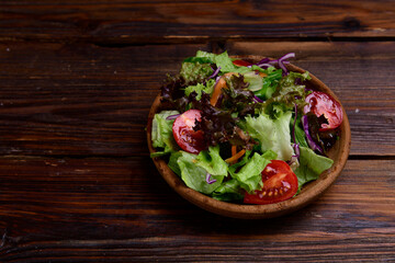 Fresh mixed green salad in bowl on wooden table. Mix of fresh salad leaves in wooden bowl