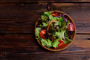 Fresh salad with mixed greens in bowl on wooden background. Tomato and mixed fresh green salad. top view