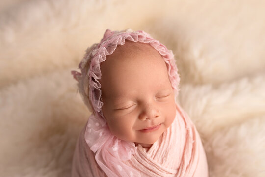 Sleeping newborn girl in the first days of life in a pink cocoon with a pink cap on a white background. Studio macro photography, portrait of a newborn baby. The concept of female happiness.
