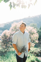 Smiling man with a bouquet of lavender in his hand stands near a blossoming tree