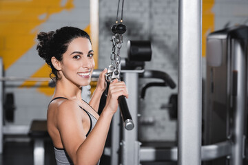 Fototapeta na wymiar Cheerful middle east sportswoman looking at camera near lat pulldown machine in gym.