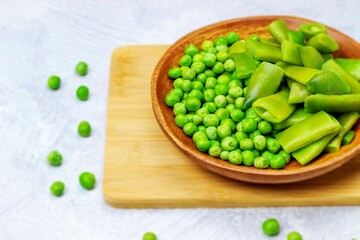 Green beans and green peas are lying on a bamboo board in a wooden bowl