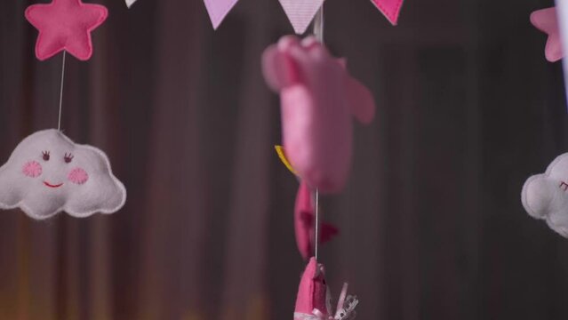 baby mobile with pink hand-stitched animal and bird toys with yellow moon on white wall background. spinning on the baby's crib in the room