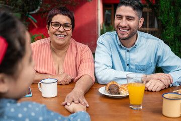 happy granny and dad talking to child and holding hand in table outside