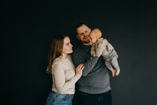 Mother and father holding newborn baby in arms. Happy young family on dark background.