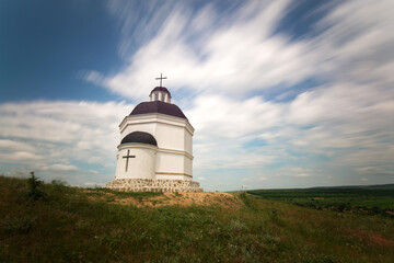 Fototapeta na wymiar Cloudcape with a small chapel on the top of the hill - long exposure