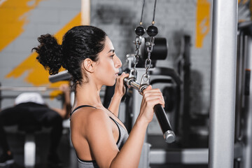 Side view of middle east sportswoman working out with lat pulldown machine in gym.
