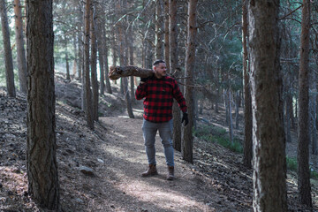 Obraz premium man in plaid shirt picking up a large log in the forest