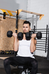 Athletic sportsman working out with dumbbells in gym.